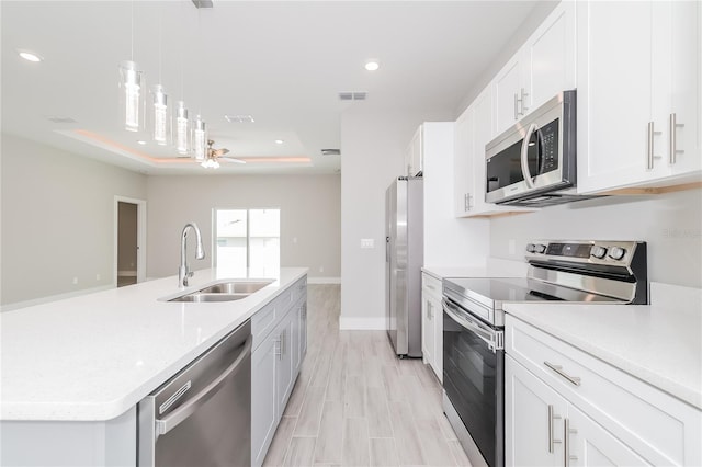 kitchen featuring white cabinets, appliances with stainless steel finishes, a kitchen island with sink, pendant lighting, and sink