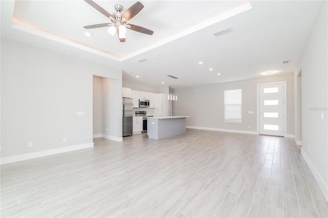 unfurnished living room with a tray ceiling, light wood-type flooring, and ceiling fan