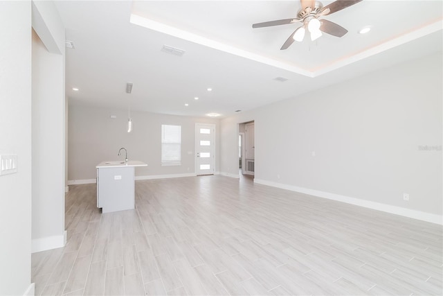 unfurnished living room with light hardwood / wood-style flooring, ceiling fan, and a raised ceiling