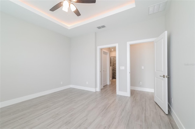 unfurnished bedroom featuring a raised ceiling, light wood-type flooring, and ceiling fan