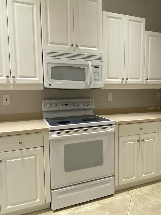 kitchen with light tile patterned floors, white appliances, and white cabinetry