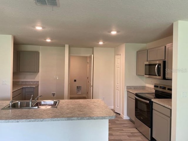 kitchen featuring a textured ceiling, sink, gray cabinetry, light hardwood / wood-style floors, and stainless steel appliances