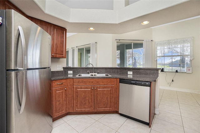 kitchen featuring stainless steel appliances, light tile patterned flooring, sink, kitchen peninsula, and dark stone countertops