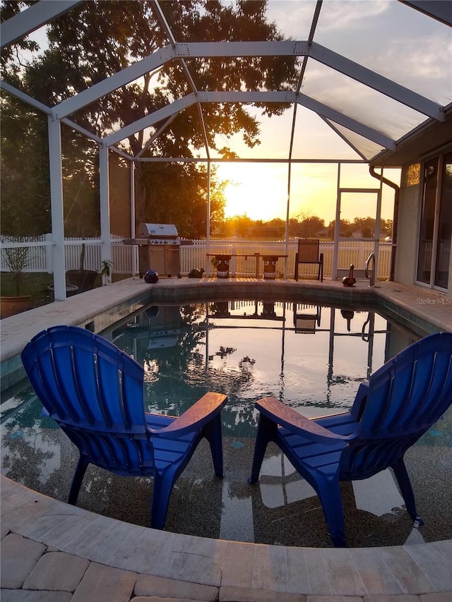 pool at dusk featuring a lanai, a grill, and a patio