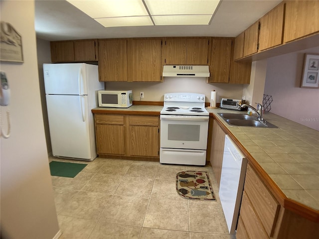 kitchen with light tile patterned floors, white appliances, sink, and tile counters