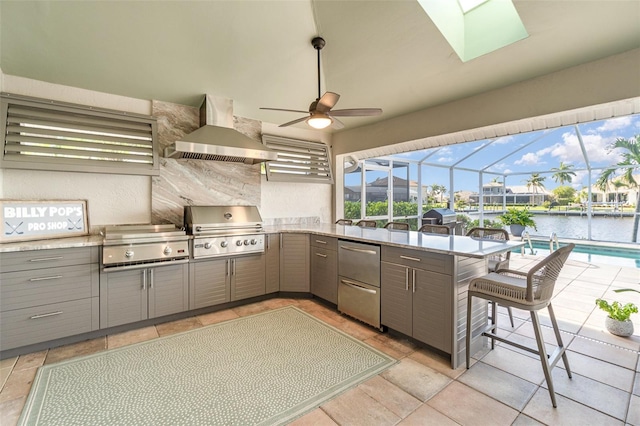 kitchen featuring wall chimney range hood, a breakfast bar area, gray cabinets, a water view, and stainless steel refrigerator