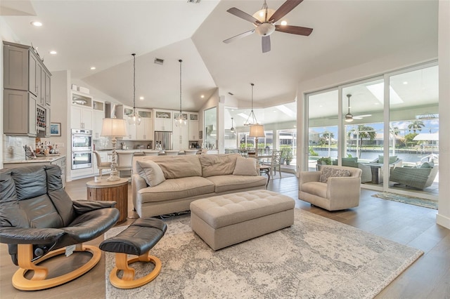 living room featuring light hardwood / wood-style flooring, ceiling fan, a water view, and vaulted ceiling