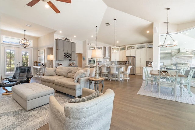 living room featuring french doors, ceiling fan with notable chandelier, high vaulted ceiling, and light hardwood / wood-style floors