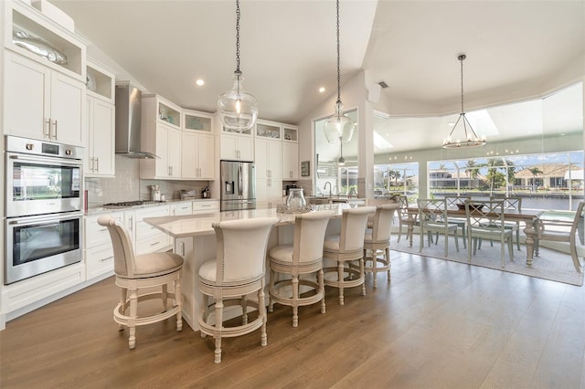 kitchen with wall chimney exhaust hood, pendant lighting, an island with sink, and stainless steel appliances