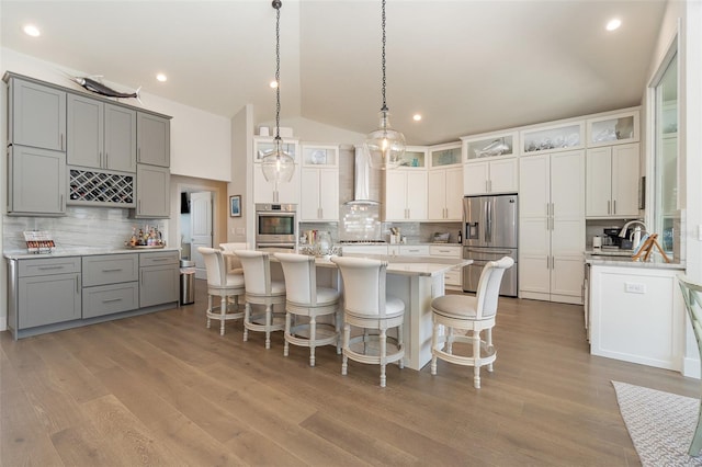 kitchen with gray cabinets, appliances with stainless steel finishes, wall chimney range hood, and a kitchen island with sink