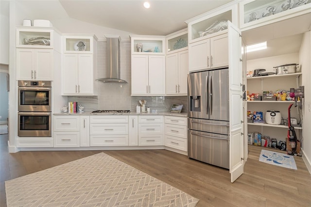 kitchen featuring wall chimney range hood, hardwood / wood-style floors, stainless steel appliances, and white cabinetry