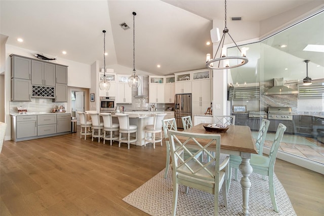 dining area featuring hardwood / wood-style floors, high vaulted ceiling, and ceiling fan with notable chandelier