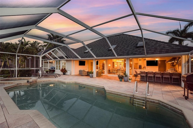 pool at dusk with an in ground hot tub, a patio area, a lanai, and an outdoor living space