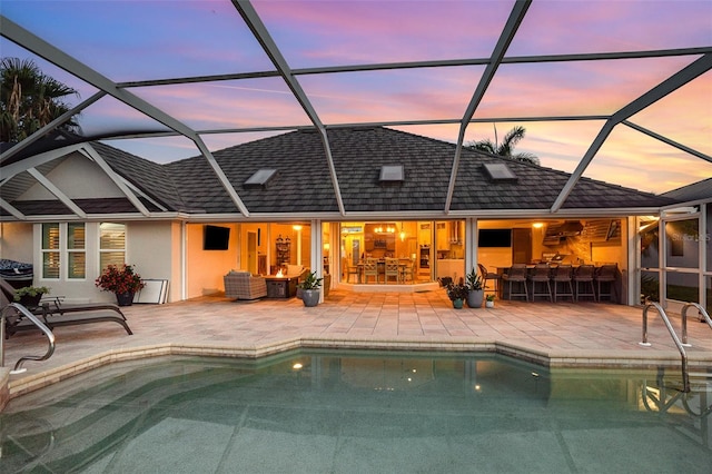 back house at dusk with an outdoor bar, a patio, and glass enclosure