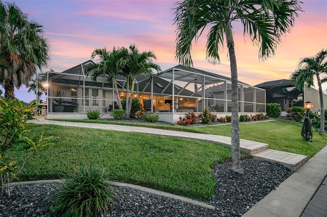 back house at dusk featuring a lawn and glass enclosure