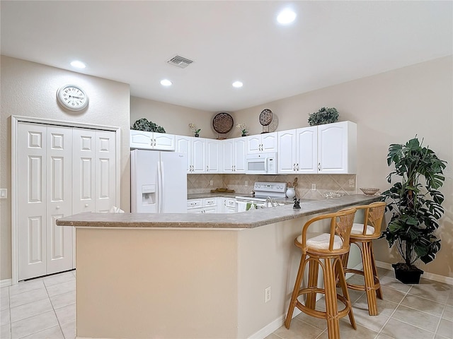 kitchen featuring kitchen peninsula, white cabinets, decorative backsplash, a kitchen breakfast bar, and white appliances