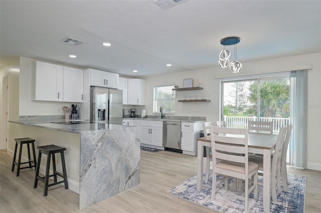 kitchen featuring light hardwood / wood-style flooring, hanging light fixtures, white cabinetry, appliances with stainless steel finishes, and light stone counters