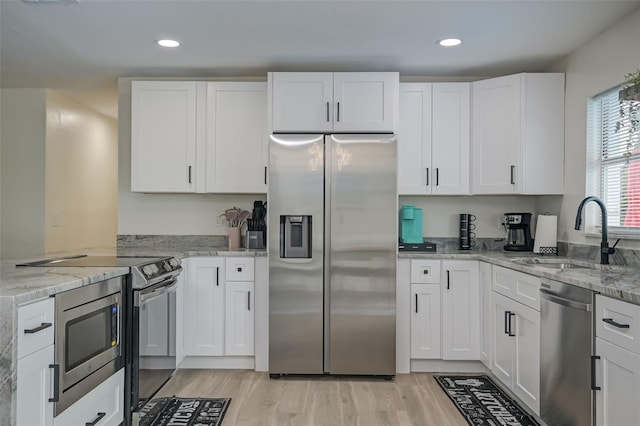 kitchen with white cabinetry, stainless steel appliances, light stone countertops, and sink