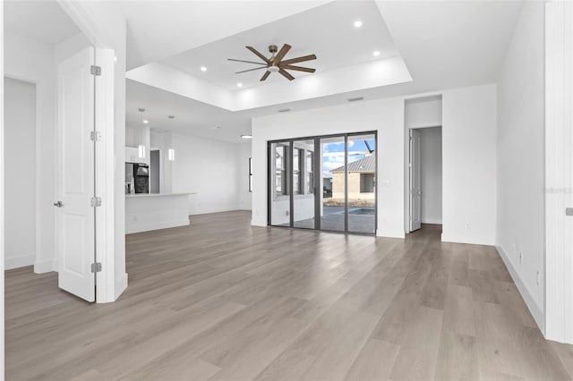 unfurnished living room with a tray ceiling, light hardwood / wood-style flooring, and ceiling fan