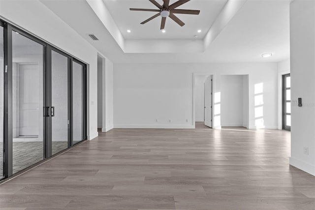 unfurnished room with light wood-type flooring, a raised ceiling, and ceiling fan