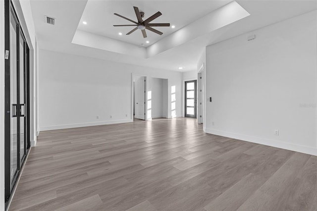 spare room featuring a raised ceiling, ceiling fan, and light hardwood / wood-style floors