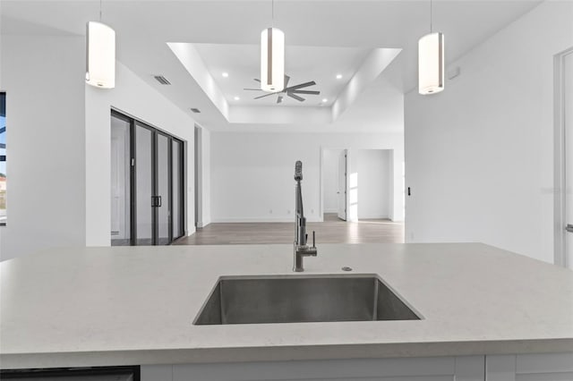 kitchen with a tray ceiling, ceiling fan, sink, and hanging light fixtures