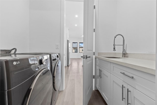 laundry area with washing machine and dryer, cabinets, sink, and wood-type flooring