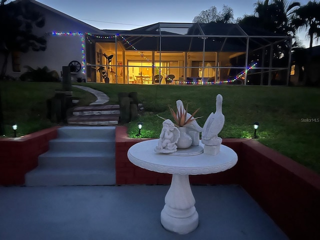 patio terrace at dusk featuring a lawn and glass enclosure