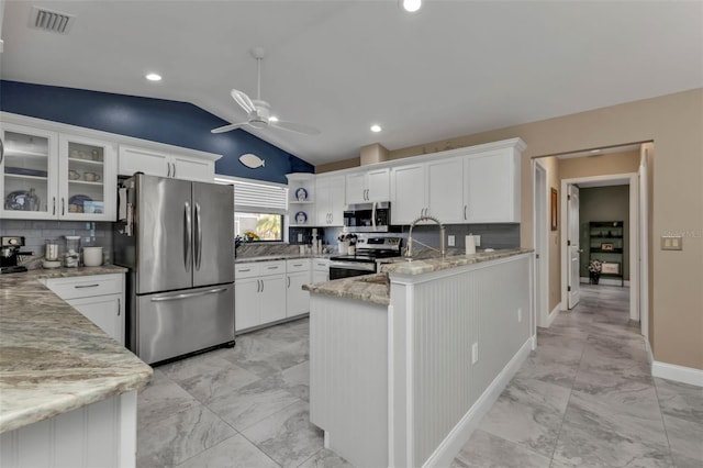 kitchen with lofted ceiling, stainless steel appliances, white cabinets, light stone counters, and tasteful backsplash