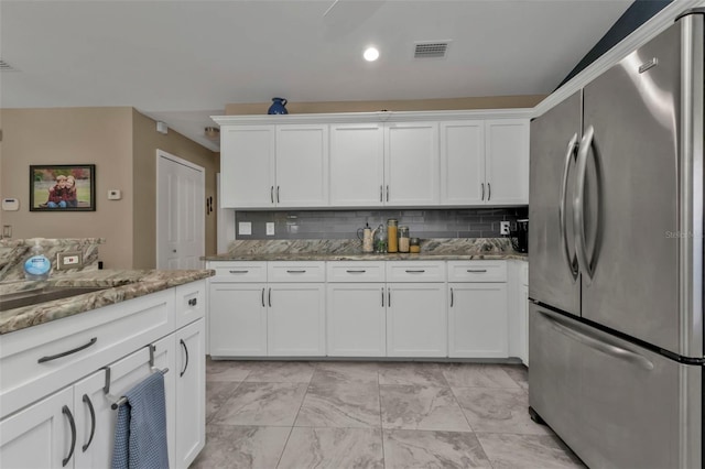 kitchen featuring white cabinetry, stainless steel fridge, light stone counters, and backsplash