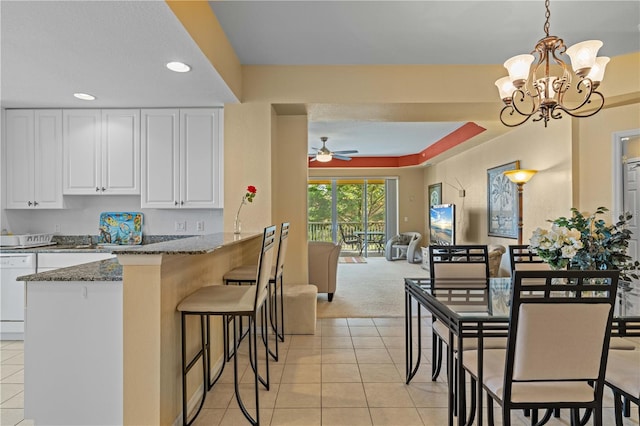 kitchen with white cabinetry, dark stone countertops, light tile patterned floors, and ceiling fan with notable chandelier