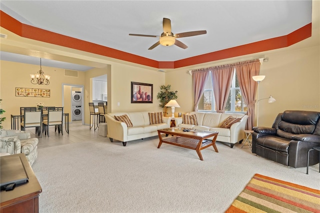 carpeted living room featuring stacked washer and dryer and ceiling fan with notable chandelier