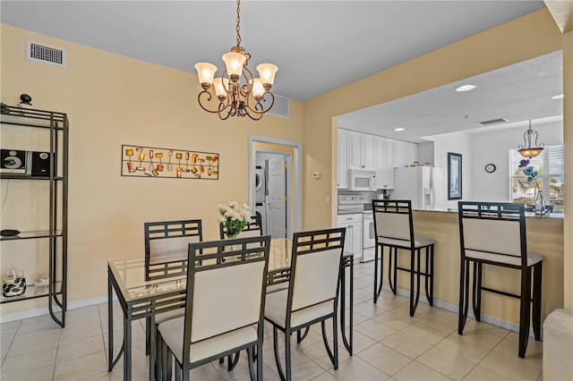 tiled dining room featuring a notable chandelier and stacked washing maching and dryer