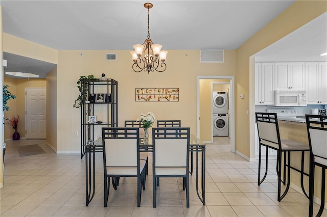 tiled dining room with a notable chandelier and stacked washer and clothes dryer