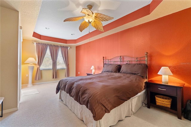 carpeted bedroom featuring a tray ceiling and ceiling fan