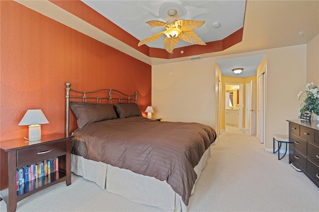 bedroom with ensuite bath, light colored carpet, a tray ceiling, and ceiling fan