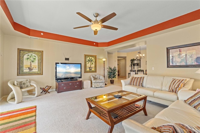 living room featuring carpet, a tray ceiling, and ceiling fan with notable chandelier