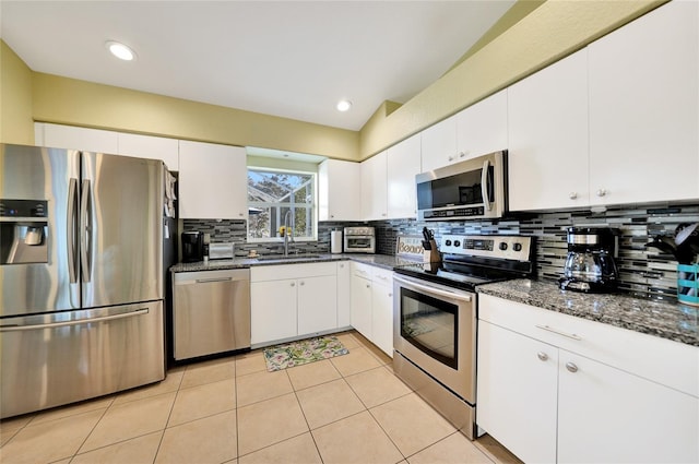 kitchen with white cabinetry, sink, stainless steel appliances, tasteful backsplash, and dark stone counters