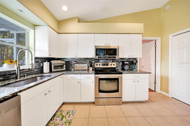 kitchen with sink, dark stone counters, vaulted ceiling, white cabinets, and appliances with stainless steel finishes