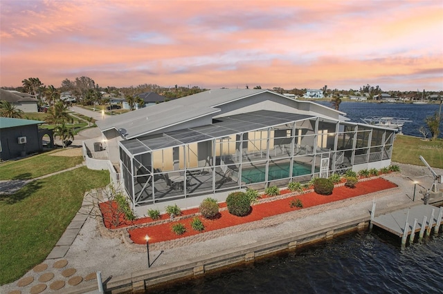 back house at dusk with a water view, a patio area, and a yard