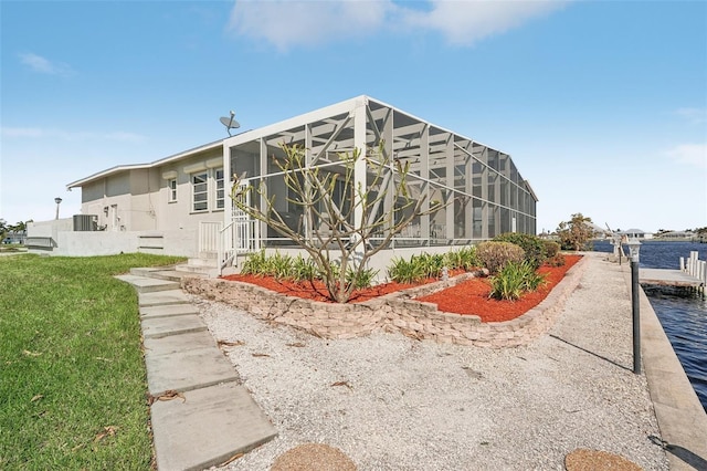 back of house with a water view, central AC, a lawn, and a lanai