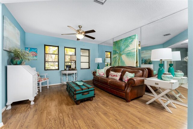 living room with ceiling fan, a textured ceiling, and light wood-type flooring