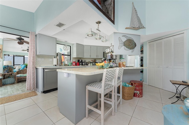 kitchen featuring light tile patterned flooring, tasteful backsplash, stainless steel dishwasher, and gray cabinetry