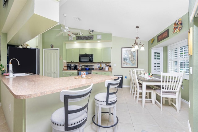 kitchen featuring a breakfast bar, black appliances, ceiling fan with notable chandelier, green cabinetry, and vaulted ceiling