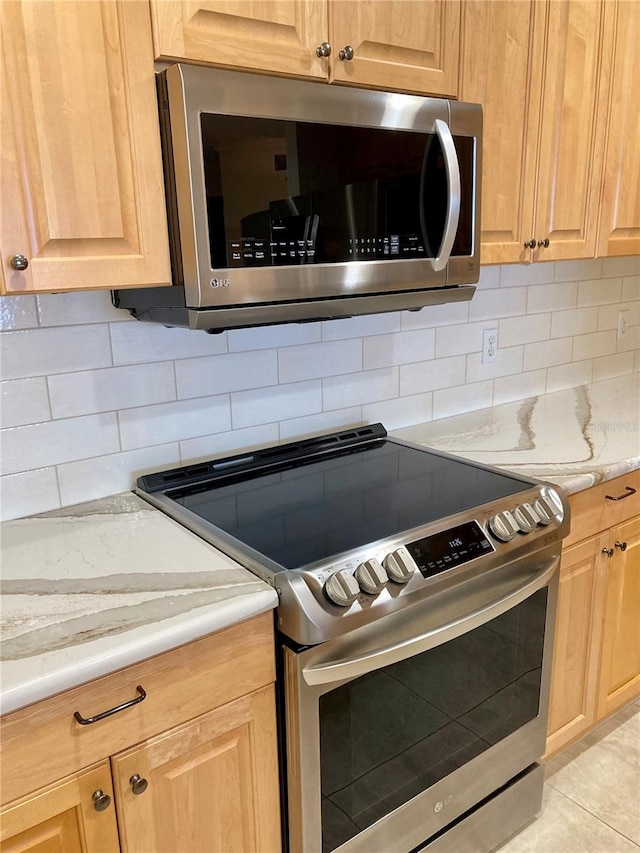 kitchen featuring light stone countertops, decorative backsplash, light tile patterned flooring, and stainless steel appliances