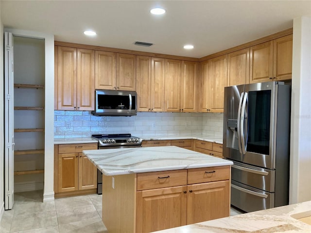 kitchen with tasteful backsplash, light stone counters, light tile patterned flooring, appliances with stainless steel finishes, and a center island