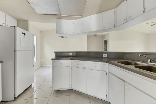 kitchen featuring white cabinetry, sink, ceiling fan, white refrigerator, and light tile patterned floors