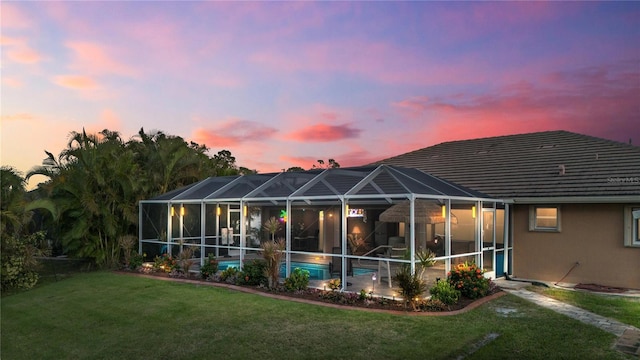 back house at dusk featuring a lawn and glass enclosure