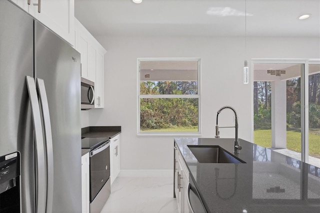 kitchen with appliances with stainless steel finishes, white cabinetry, dark stone countertops, and sink