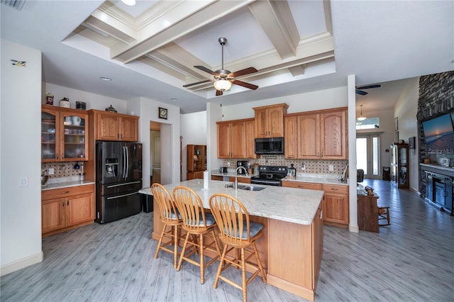 kitchen featuring a center island with sink, a kitchen bar, light wood-type flooring, black appliances, and sink